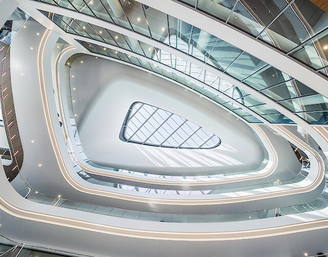Geschwungenes Atrium mit umlaufenden Lichtlinien, Glasdach und weichen, fließenden Raumformen