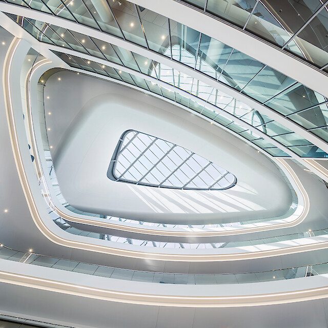 Geschwungenes Atrium mit umlaufenden Lichtlinien, Glasdach und weichen, fließenden Raumformen