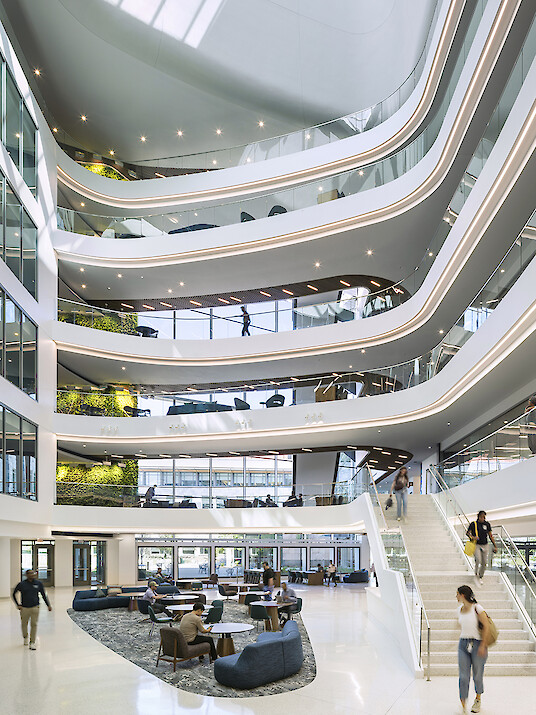 A multi-story atrium with curved galleries, integrated lighting strips, a staircase, and people moving about