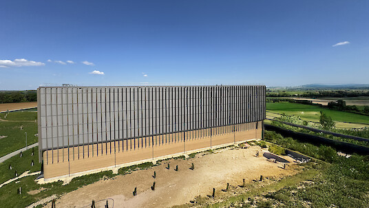 Bâtiment allongé en terre crue situé dans un paysage ouvert, avec une façade clairement structurée