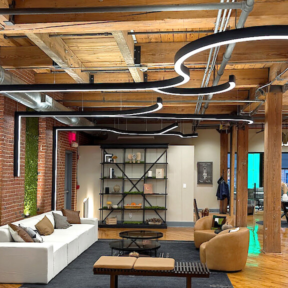 Open lounge area with brick walls, timber beams and curved linear pendant luminaires.