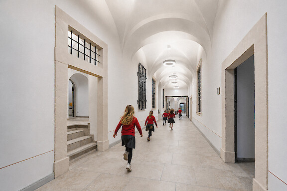 Alumnas en un pasillo histórico de una escuela con luminarias suspendidas Ringo Star.
