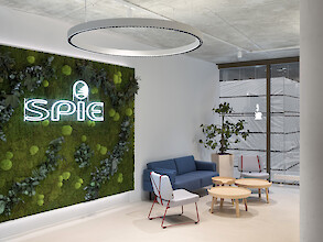 Zona de descanso con conjunto de sofás, panel mural con vegetación, letrero luminoso y lámpara colgante circular