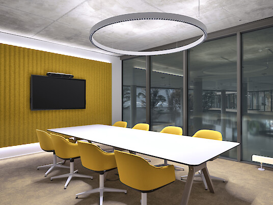Sala de reuniones con mesa, sillas amarillas, pared acústica y lámpara colgante circular frente a una fachada acristalada