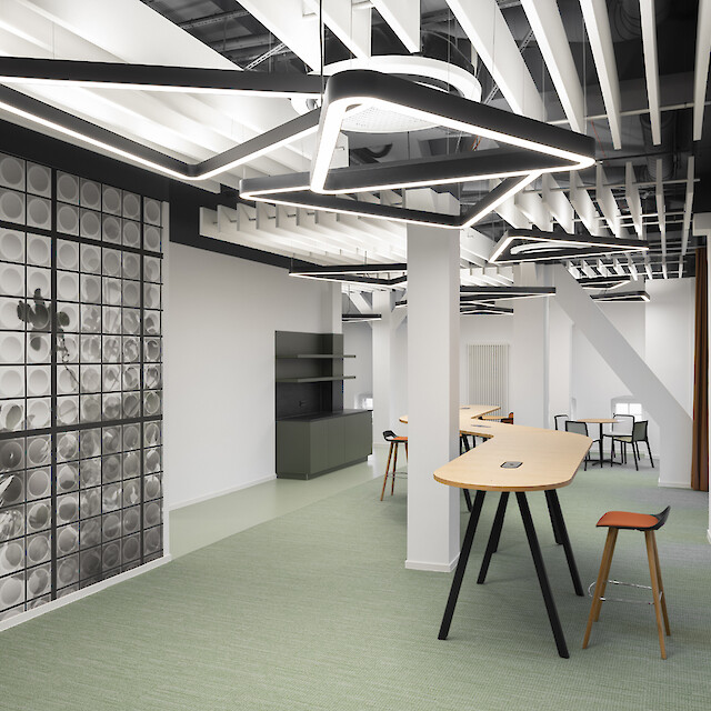 Agence bancaire avec des espaces de consultation, un papier peint photo, un coin salon et des suspensions triangulaires au-dessus des tables