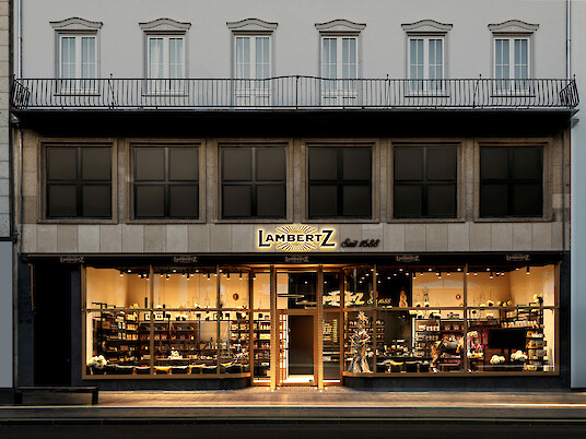 Historische Geschäftsfassade des Lambertz Stores mit beleuchteten Schaufenstern bei Dämmerung