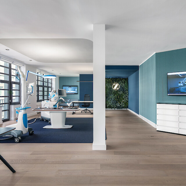 Offener medizinischer Innovationsraum mit Präsentationsflächen, türkisfarbenen Wänden und dezent integrierter architektonischer Beleuchtung