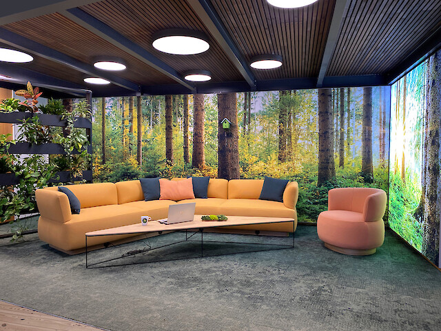 Loungebereich mit Waldmotiv, runden Deckenleuchten, Sofa, Sessel und Pflanzenwand