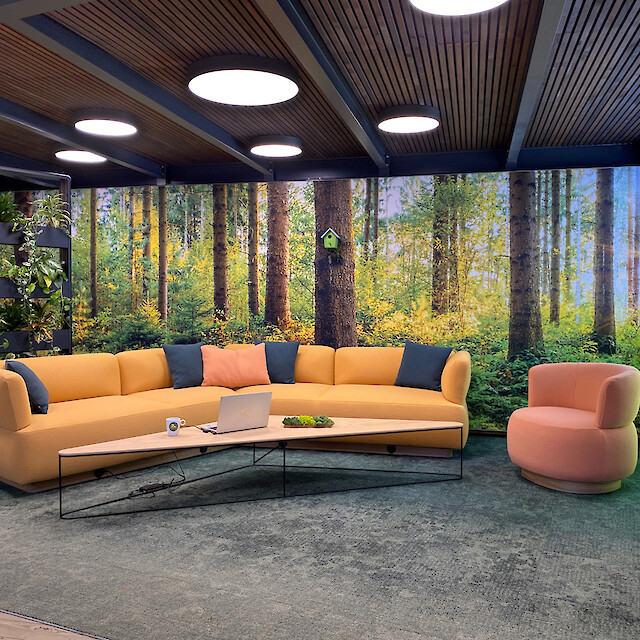 Lounge area with a forest theme, round ceiling lights, a sofa, armchairs and a living wall