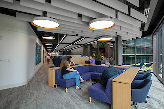 An open-plan office with a seating area, round pendant lights, and staff engaged in conversation