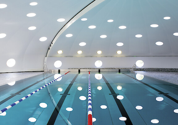Swimming pool with marked lanes, curved ceiling and round Basic surface-mounted luminaires.
