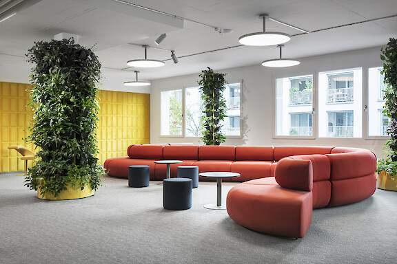 Bright lounge area with red sofa, lush greenery and circular ceiling luminaires.