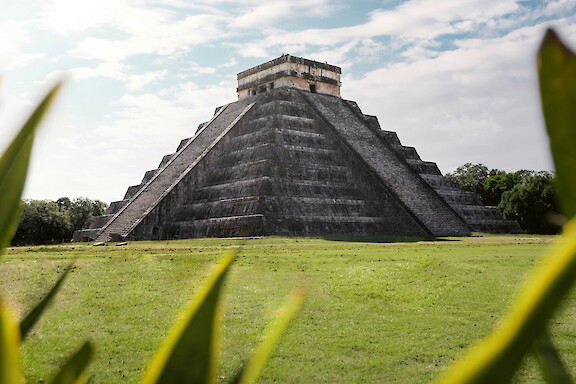 Historic Maya pyramid rising above a green lawn beneath a cloudy sky.