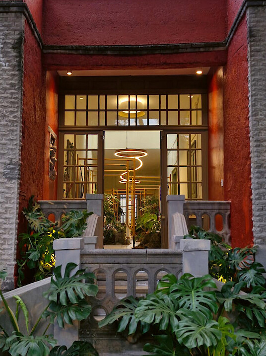 Historic courtyard with lush plants and glowing ring lights behind large windows.