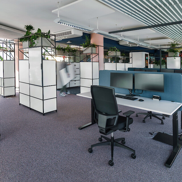 Oficina diáfana con puestos de trabajo, separadores con plantas y luminarias colgantes lineales