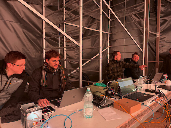 Four men working with laptops and technical equipment on a temporary installation.