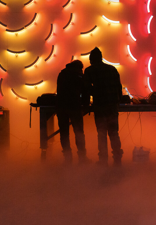 Two people in front of a wall of illuminated, coloured circular segments.