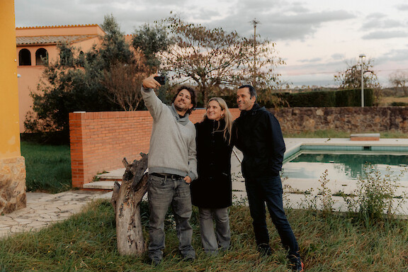 Three people stand together in a garden, with one raising an arm.