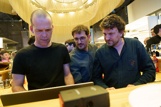 Three men looking at a screen together in a workshop with warm lighting.