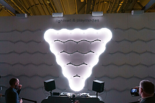Glowing installation forms a bright triangular shape against a patterned wall.