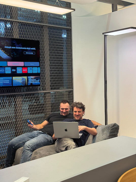 Two men sitting on a sofa and working together on a laptop.