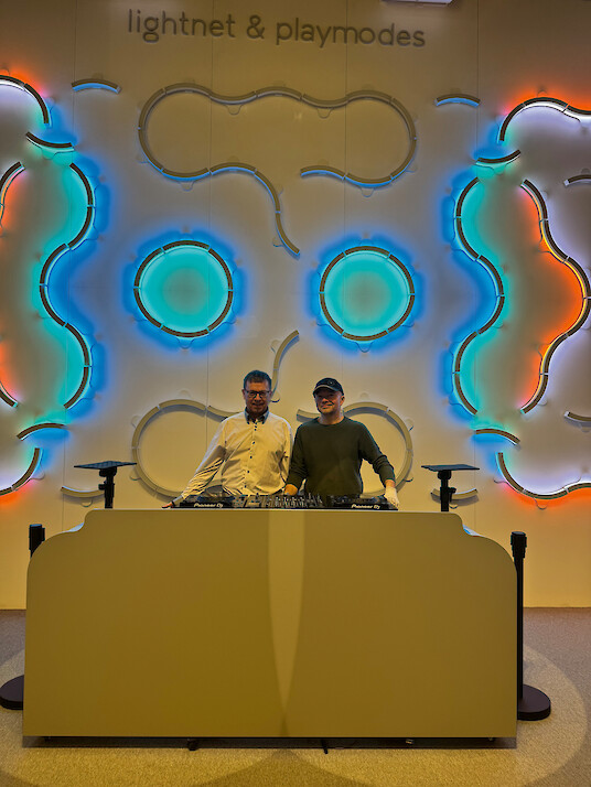 Two men standing in front of an installation with colourful glowing organic shapes.