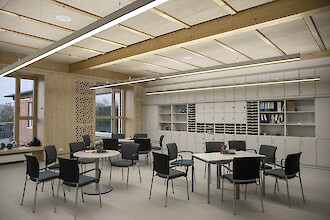 Bright school room with timber elements, flexible seating groups and long linear pendant luminaires