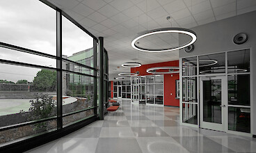 Bright school corridor with large windows, red accents and ring-shaped pendant lights in varying sizes