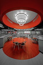 School cafeteria with red seating areas and multiple ring-shaped pendant lights in varying sizes