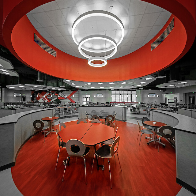 School cafeteria with red seating areas and multiple ring-shaped pendant luminaires in varying sizes