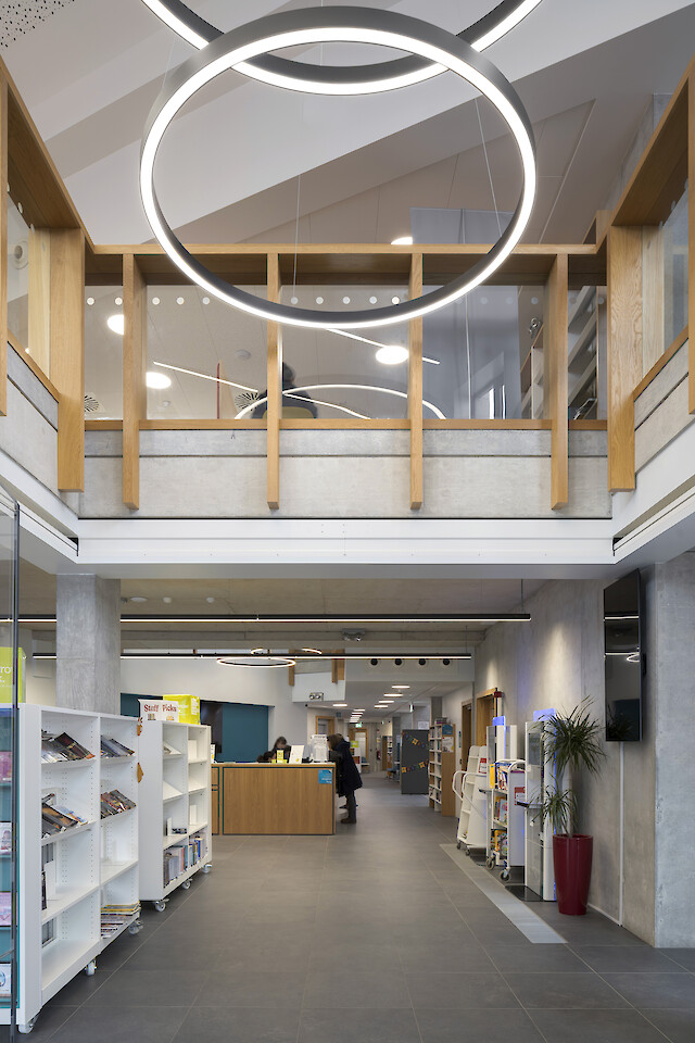 Open library area with bookshelves, gallery and distinctive ring-shaped pendant luminaires