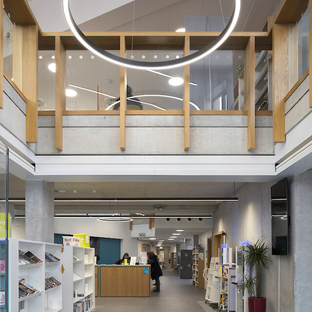 **Deutsch:**
Offener Bibliotheksbereich mit Bücherregalen, Galerie und markanten ringförmigen Pendelleuchten.

