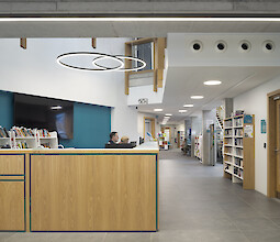 Library with reception desk, bookshelves and several ring-shaped pendant luminaires