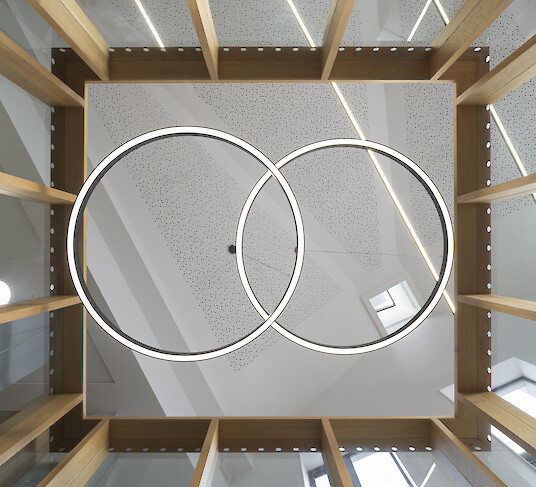 Two overlapping ring-shaped pendant luminaires in an open atrium with timber elements