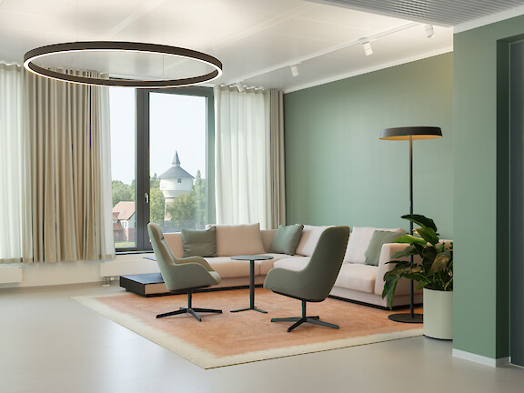 Bright lounge area with pastel-coloured furniture, green wall and large ring-shaped pendant luminaire.