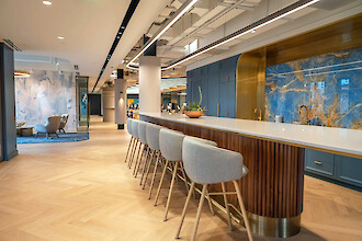Zona común abierta de una empresa en Boston con una barra alargada, paneles de pared azules y luminarias suspendidas lineales Liquid Line PX.