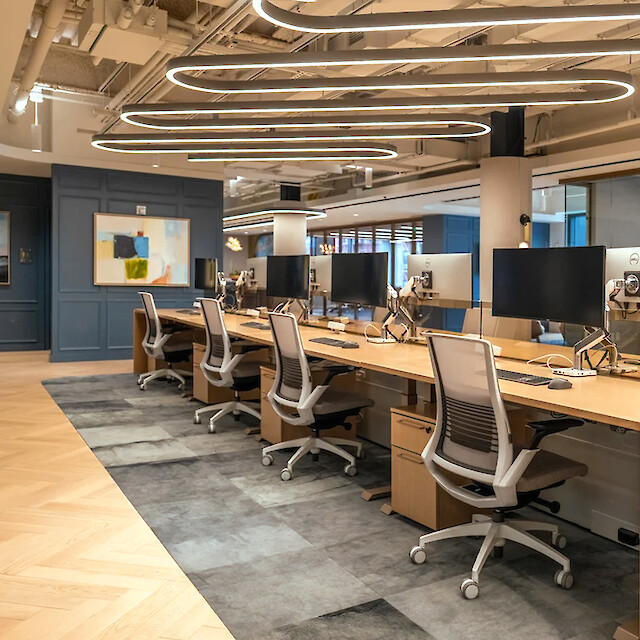 Oficina diáfana en Boston con largas mesas de madera, varios puestos de trabajo y luminarias suspendidas curvas Liquid Line PX.