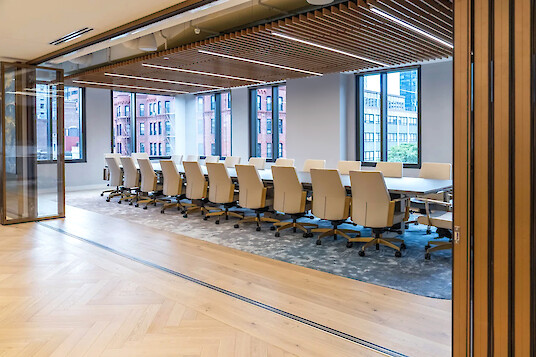 Amplia sala de conferencias en Boston con una larga mesa de reuniones, sillas claras e iluminación lineal Matric GX entre lamas de madera en el techo.