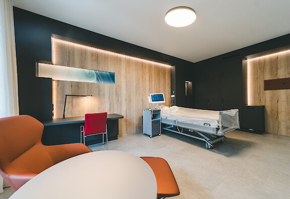Patient room at the Clinic for Manual Therapy in Hamm with a round ceiling luminaire by Lightnet, wood paneling and indirect wall lighting.