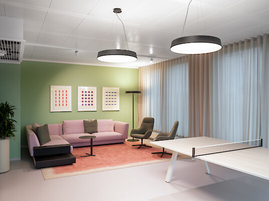 Lounge with a sofa, armchairs and a table tennis table beneath two round pendant luminaires, with a green wall and floor-length curtains.