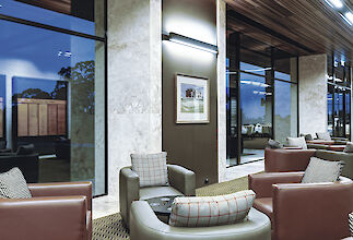 Salón con sillones de cuero, iluminación de pared, columnas de mármol y grandes ventanales con vistas al exterior.