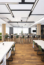 Restaurante con suelo de madera, mobiliario moderno en verde y blanco y luminarias lineales en el techo.