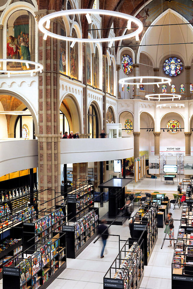 Modern bookshop in a converted church with high arches, stained glass windows and large, ring-shaped pendant luminaires.
