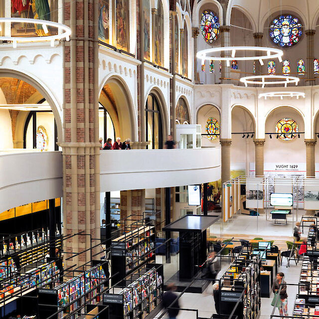 Moderna librería situada en una iglesia reconvertida, con altos arcos, vidrieras y grandes luminarias suspendidas en forma de anillo.