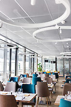 Restaurante con grandes ventanales, mobiliario elegante y luminarias suspendidas LED en forma de anillo con focos.