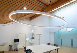 Oval pendant luminaire above a white meeting table in a room with a wooden floor and ceiling.