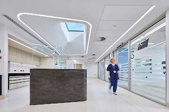 Pasillo de hospital con líneas de luz LED de forma orgánica en el techo, mostrador de recepción y cuidador ambulante