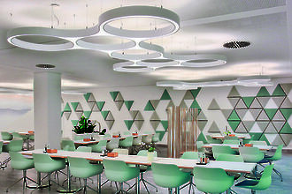 Cafeteria mit skulpturalen, ringförmigen Pendelleuchten und geometrischer Wandgestaltung in Pastellfarben.
