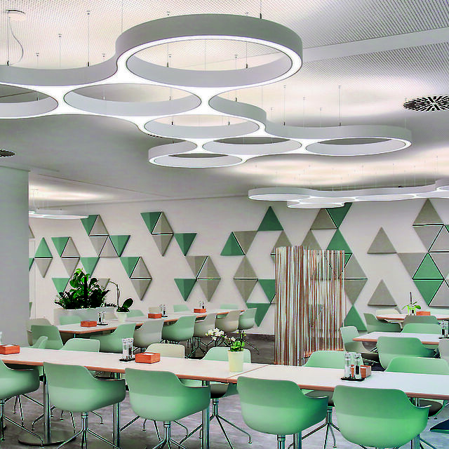Cafeteria with sculptural, ring-shaped pendant luminaires and geometric wall design in pastel colours.