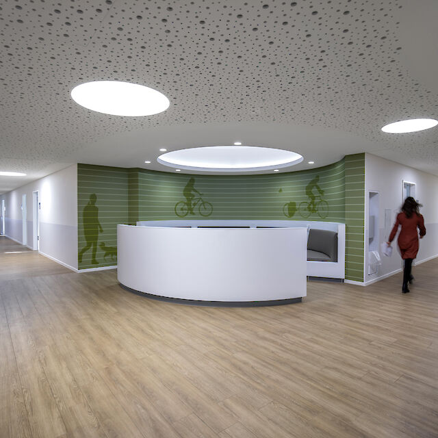 Reception area with round counter, wood-effect flooring, green wall graphics and round ceiling luminaires.
